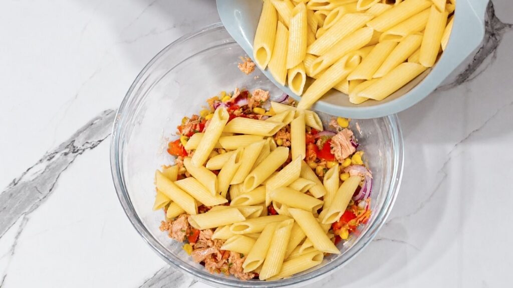 Adding cooked pasta to the prepared vegetables and tuna in a mixing bowl