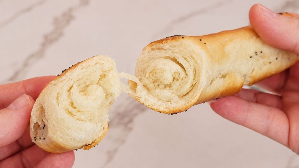 A close-up of hands holding and pulling apart a soft homemade crescent roll to reveal its fluffy, airy interior.