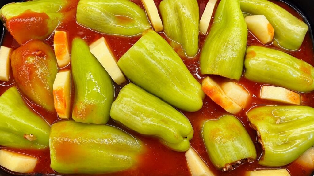 Stuffed bell peppers arranged in a baking dish with sliced potatoes, ready to bake for a homemade stuffed peppers recipe.