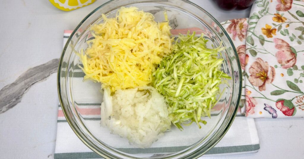 Grated zucchini, potatoes, and onion in a large mixing bowl