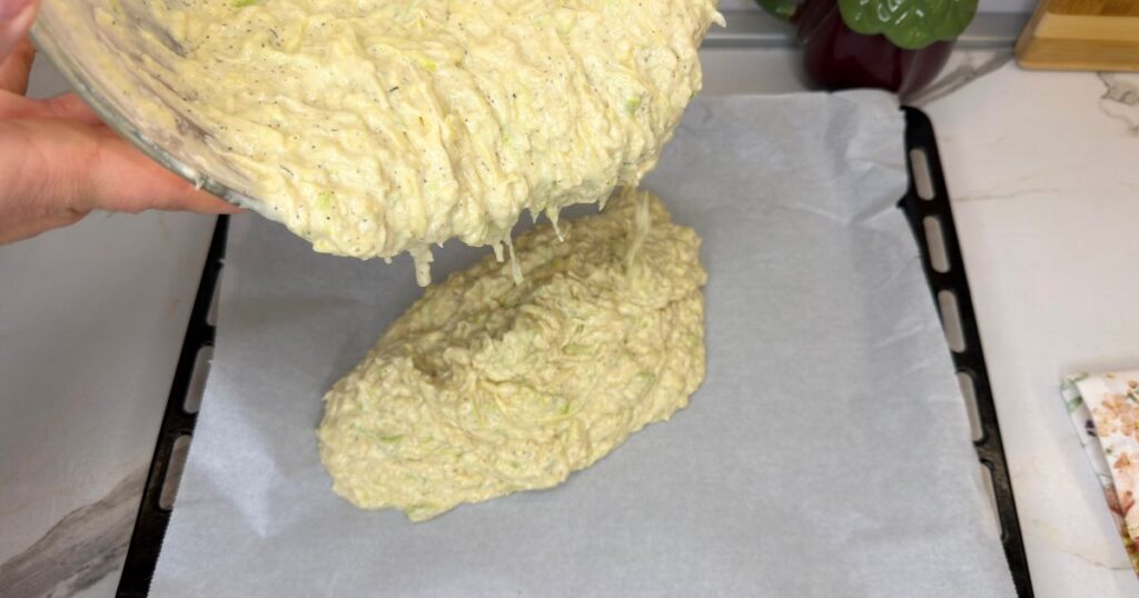 Pouring the zucchini and potato batter into a parchment-lined baking sheet