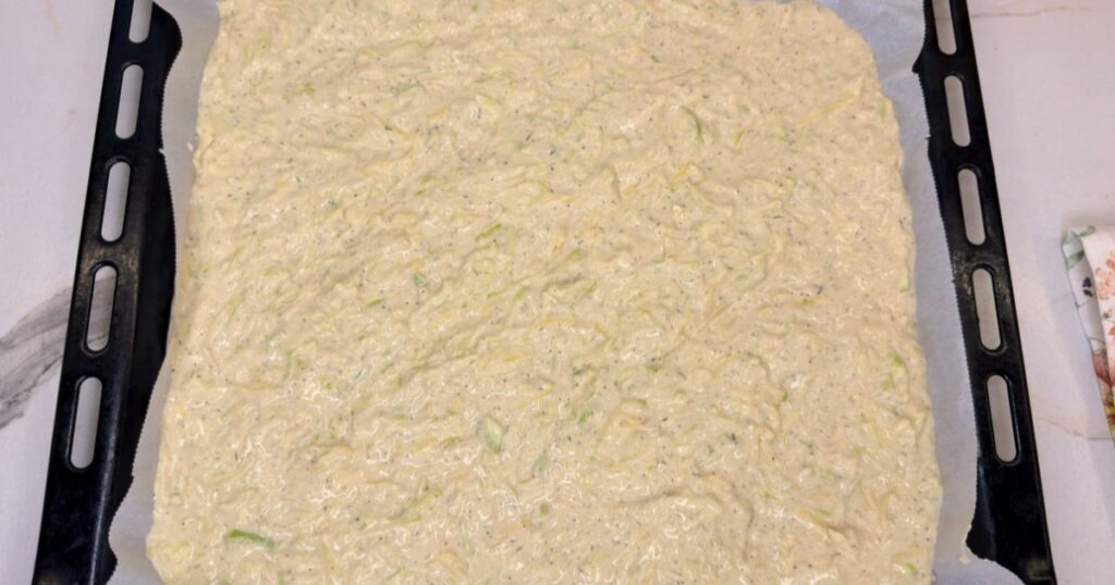 Zucchini and potato batter spread in a baking sheet and ready to bake