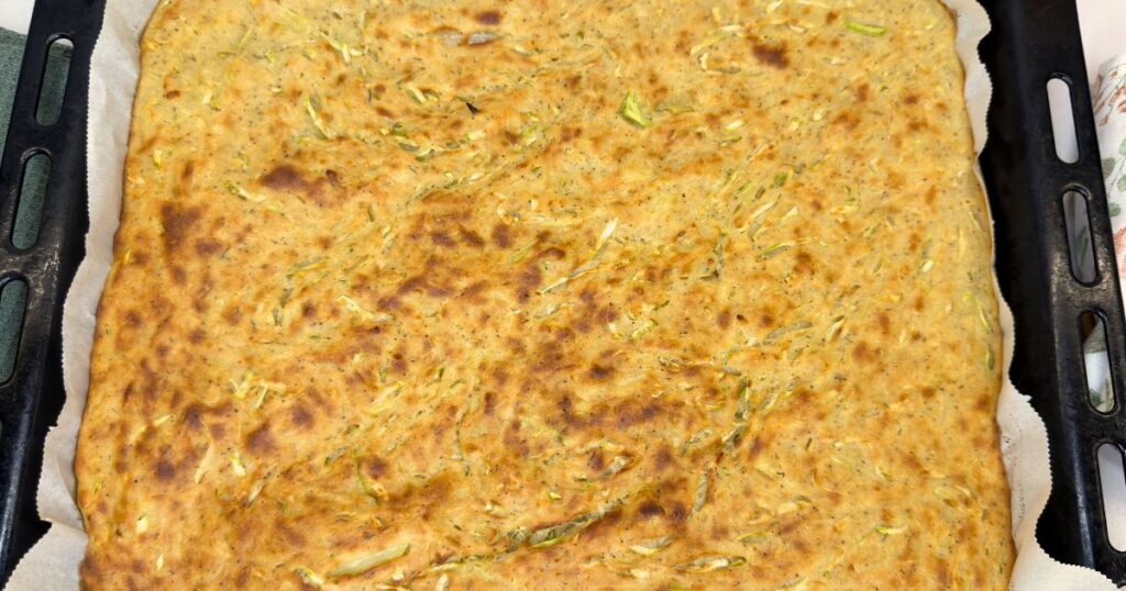Golden zucchini and potato slice cut into squares on a parchment-lined baking sheet