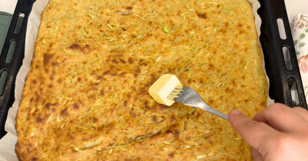 Golden zucchini and potato slice cut into squares on a parchment-lined baking sheet