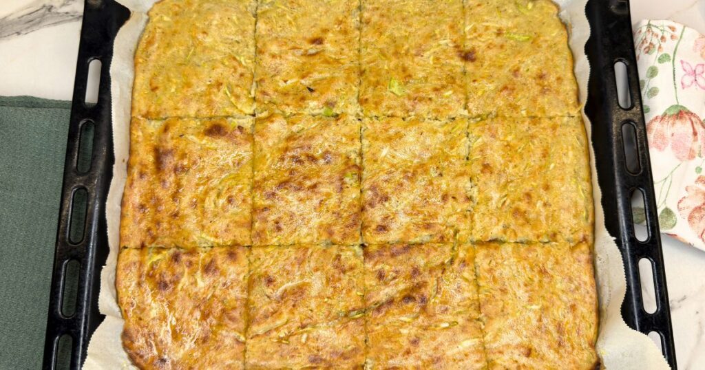 Golden zucchini and potato slice cut into squares on a parchment-lined baking sheet