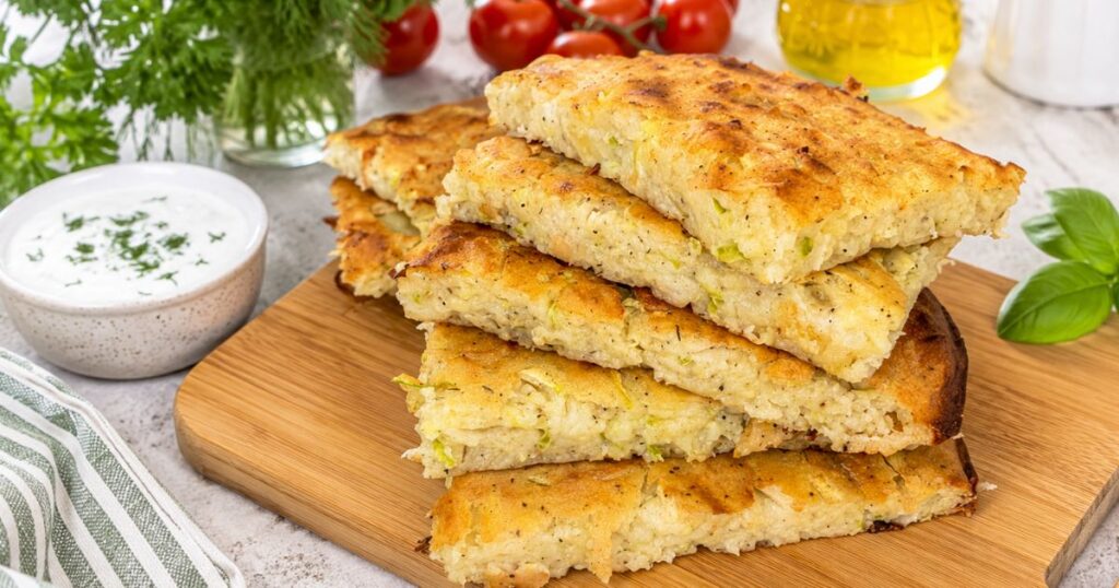 Golden zucchini and potato slices stacked on a wooden serving board with creamy dipping sauce