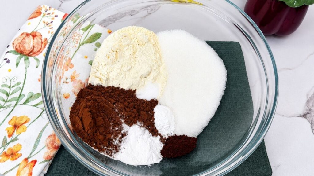 A bowl filled with the dry ingredients for Moist Chocolate Zucchini bread, featuring flour, dark cocoa powder, sugar, and chocolate chunks before being mixed.