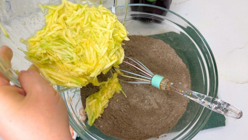 Gently folding the dry ingredients into the wet mixture in a large bowl to form a thick, rich batter for Moist Chocolate Zucchini bread.
