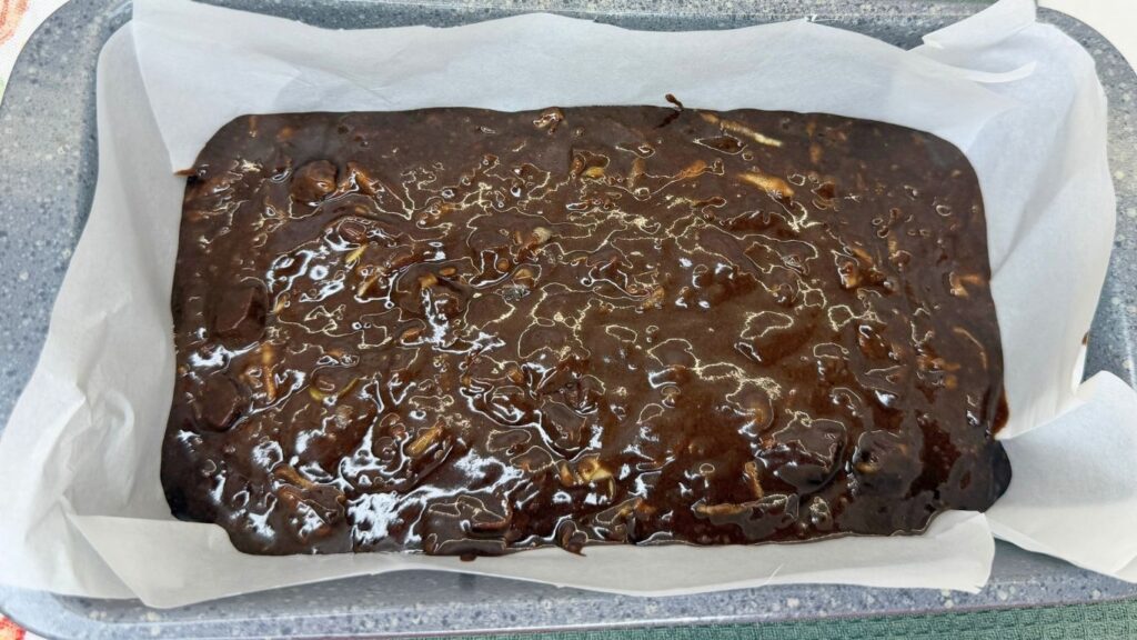 A loaf pan lined with parchment paper, filled with chocolate batter and topped with extra chocolate chunks, ready to be baked into Moist Chocolate Zucchini bread.