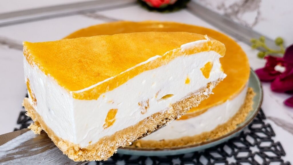 Easy no-bake peach yogurt cake piece lifted on a knife, showing creamy peach yogurt filling, biscuit crust, and smooth peach topping.