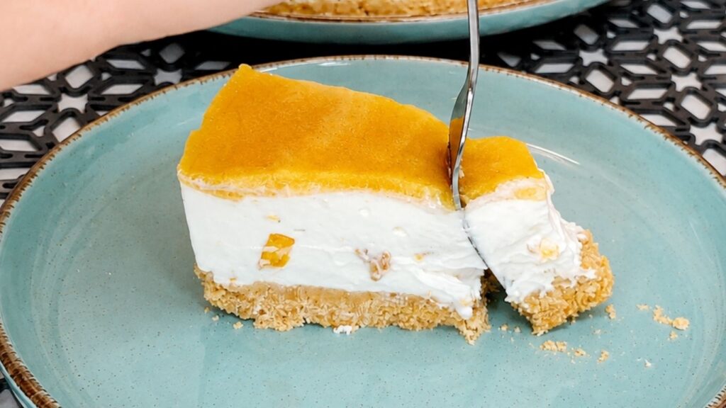Fork cutting into a slice of easy no-bake peach yogurt cake with creamy peach filling, biscuit crust, and peach topping.