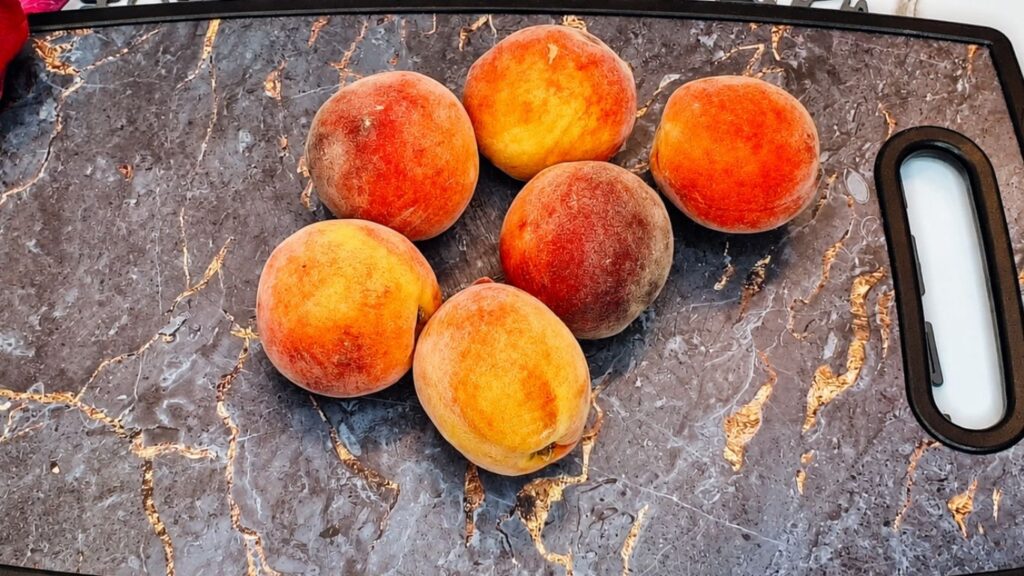 Fresh ripe peaches on a cutting board ready to be peeled and sliced for easy no-bake peach yogurt cake.