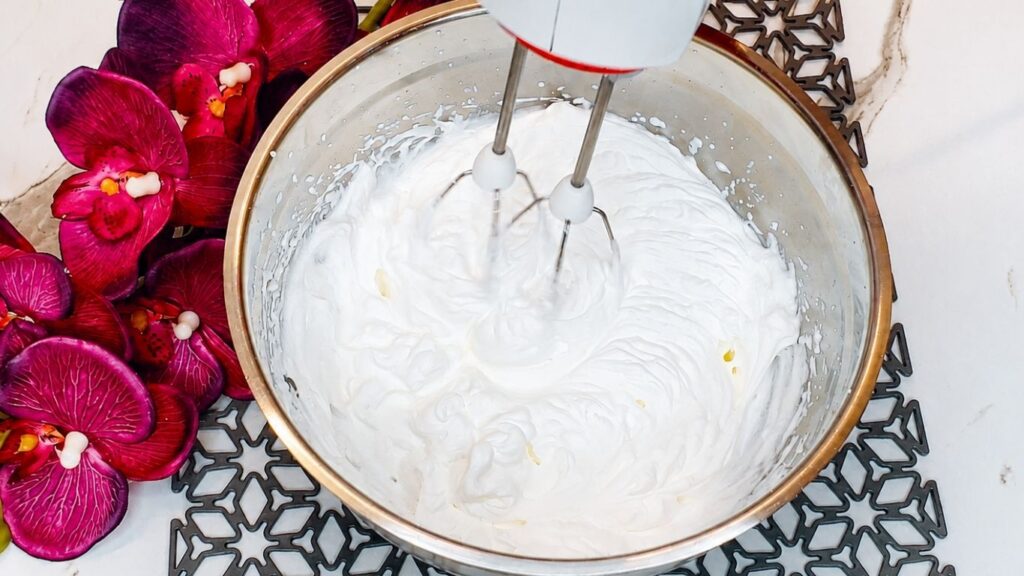 Cold whipping cream whipped until fluffy in a bowl for easy no-bake peach yogurt cake filling.