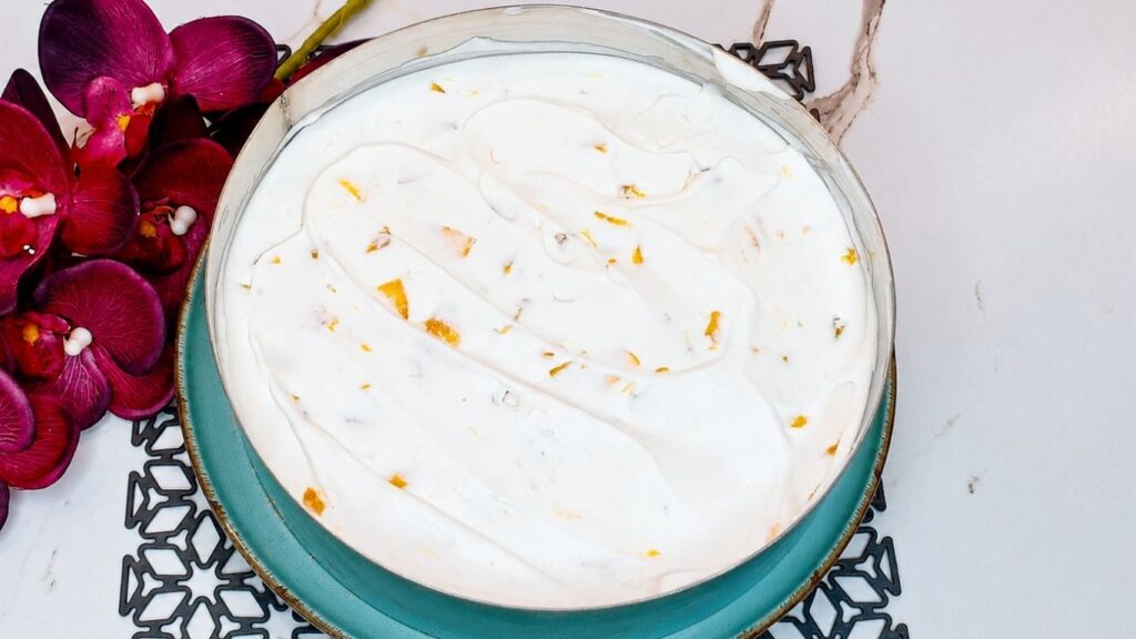 Creamy peach yogurt filling spread over the biscuit crust in a cake pan for easy no-bake peach yogurt cake.