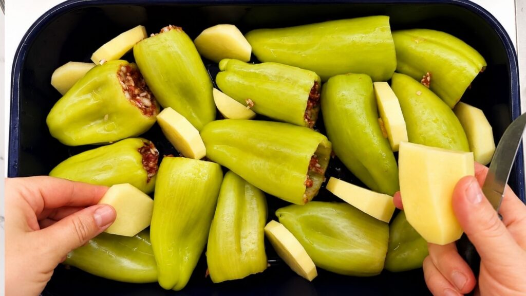 Stuffed bell peppers arranged in a baking dish with sliced potatoes, ready to bake for a homemade stuffed peppers recipe.