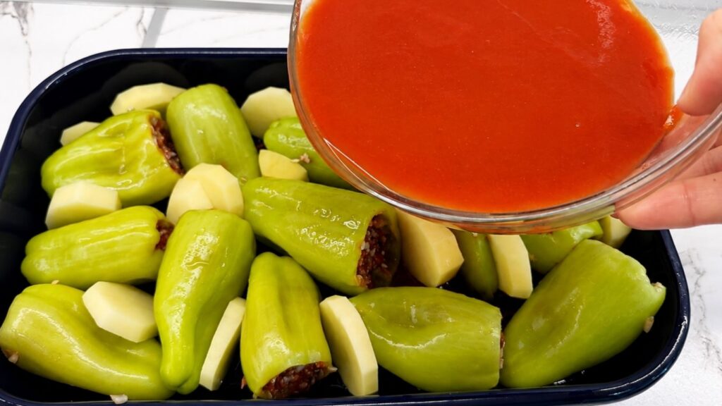 Pouring tomato sauce over stuffed bell peppers and potatoes before baking this homemade stuffed peppers recipe.