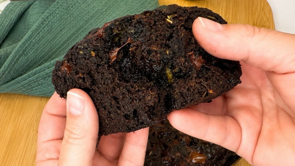 A pair of hands breaking open a large chunk of Moist Chocolate Zucchini bread, revealing its super soft and fudgy center filled with melted chocolate pieces.