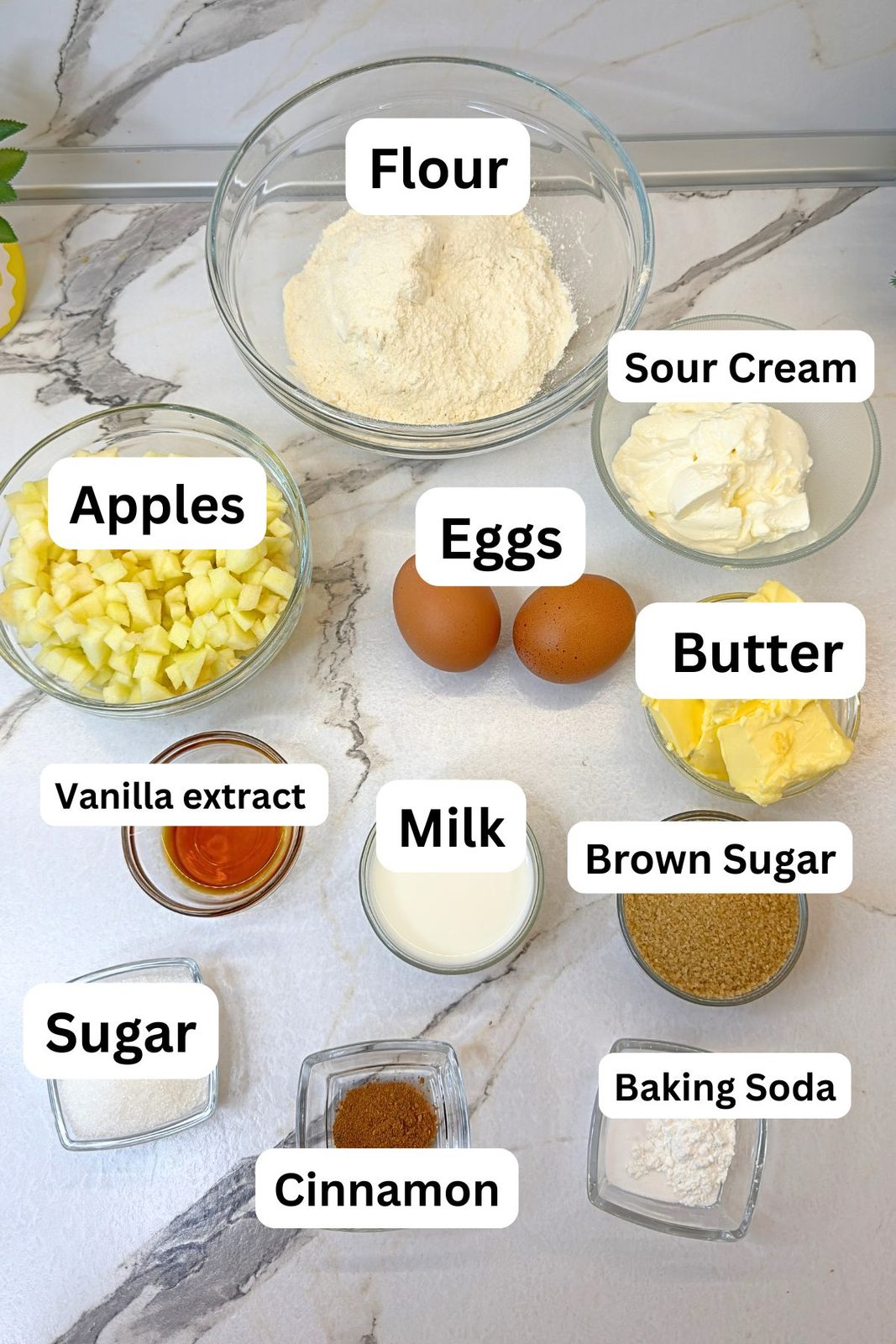 Ingredients for apple crumb muffins, including flour, diced apples, sour cream, eggs, butter, sugars, milk, vanilla, and cinnamon.