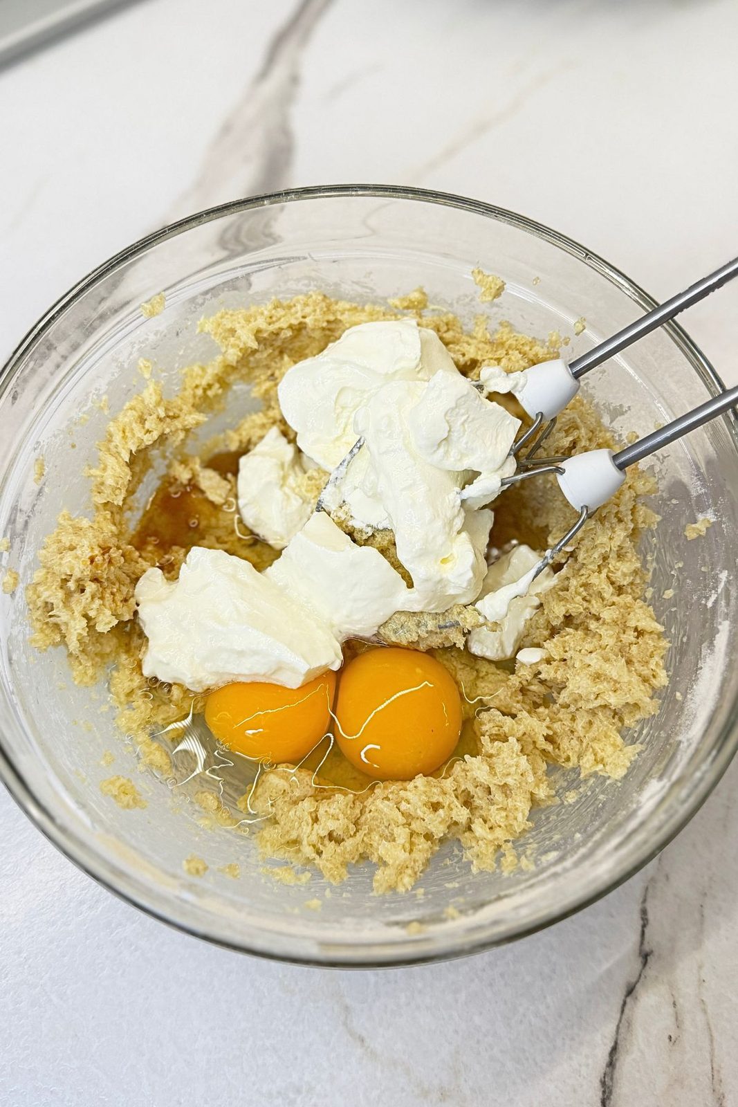 Eggs, sour cream, and vanilla added to creamed butter and sugar for apple crumb muffin batter.
