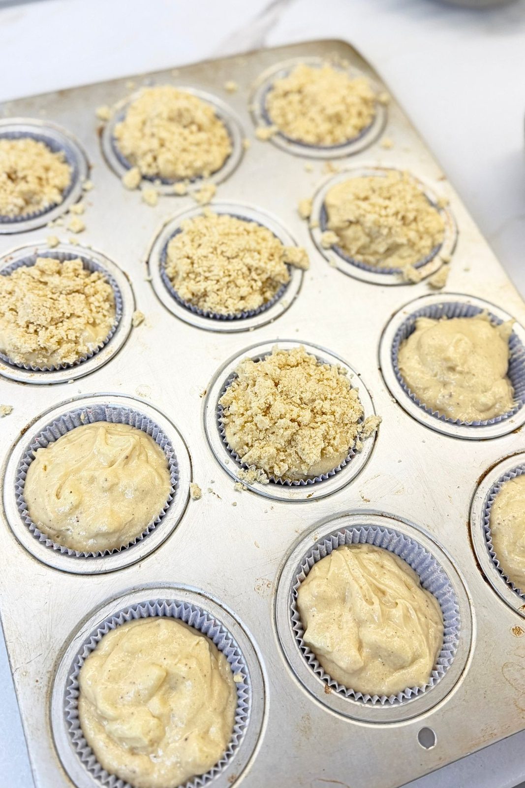 Apple muffin batter divided among paper liners and topped with buttery crumbs before baking.