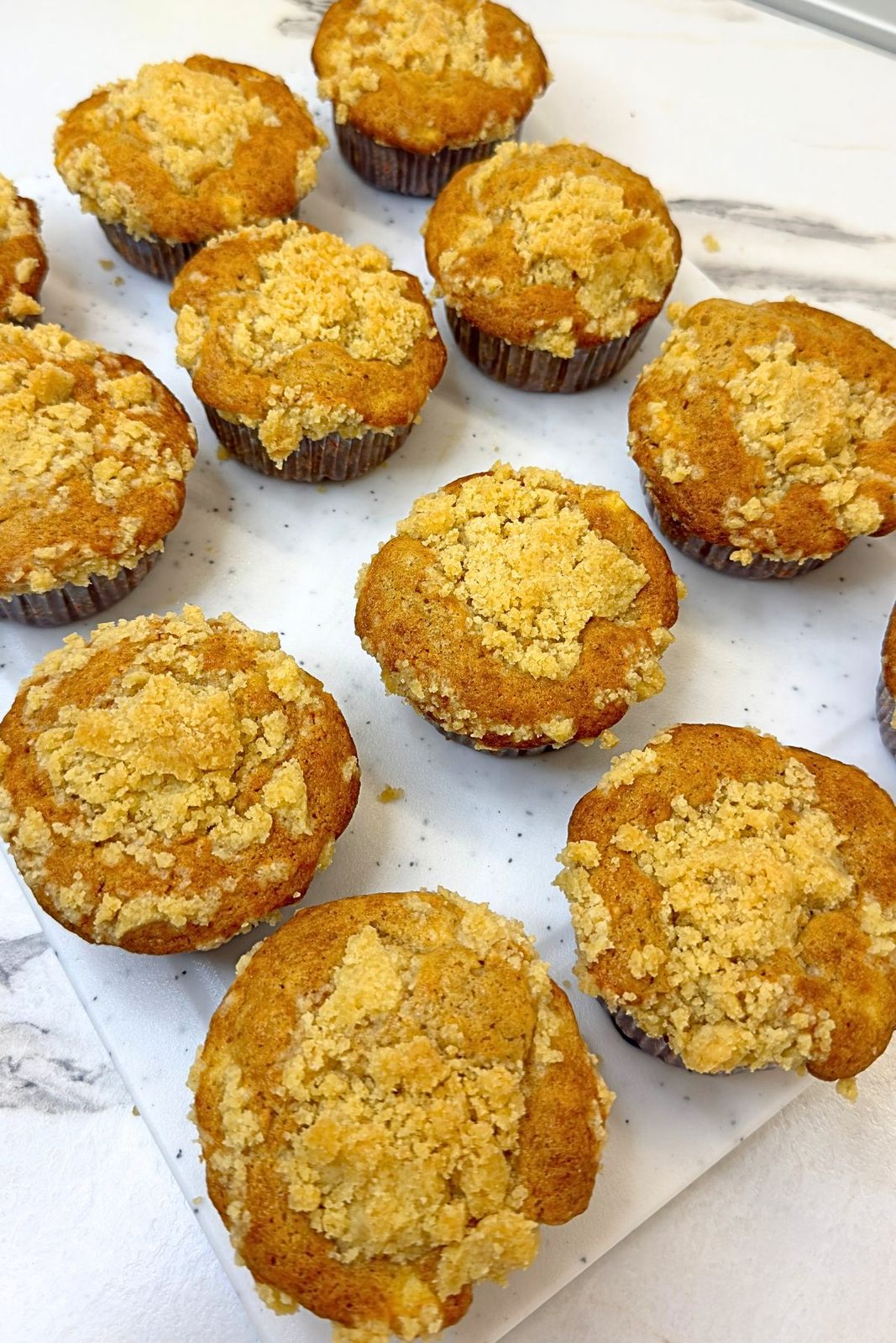 Freshly baked apple crumb muffins with golden tops cooling before vanilla icing is added.