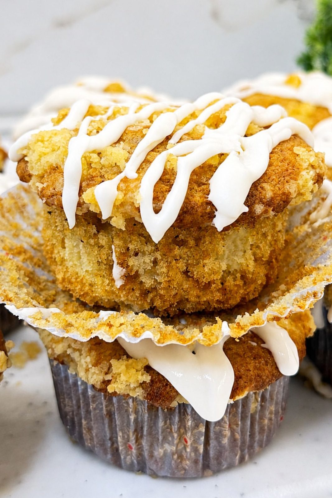Close-up of an apple crumb muffin with a golden cinnamon top, buttery crumbs, and vanilla icing.