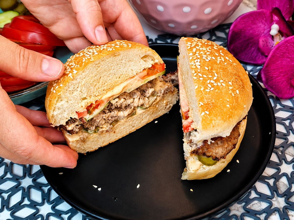 Juicy homemade burger held open to show the beef patty, creamy sauce, and fresh vegetables