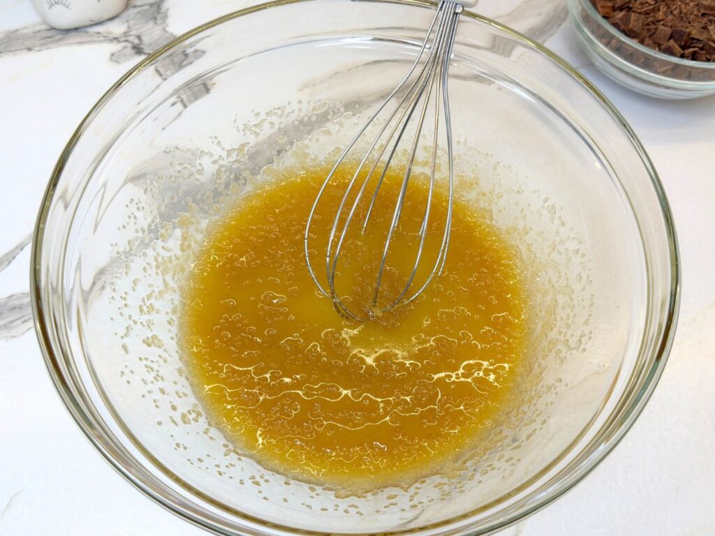 Melted butter, brown sugar, granulated sugar, egg, egg yolk, and vanilla mixed in a glass bowl.