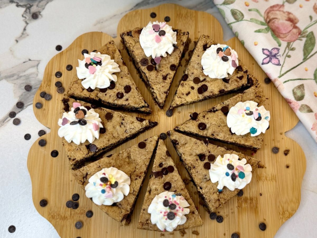 Chocolate Chip Cookie Cake cut into eight slices and decorated with whipped cream and sprinkles.