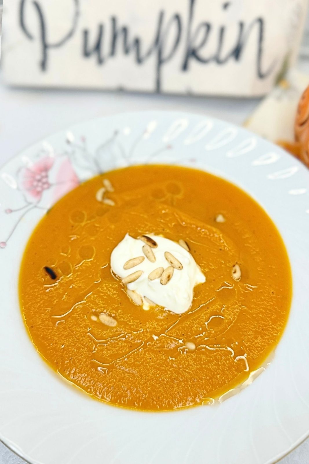 Smooth creamy pumpkin soup served with sour cream and toasted pine nuts