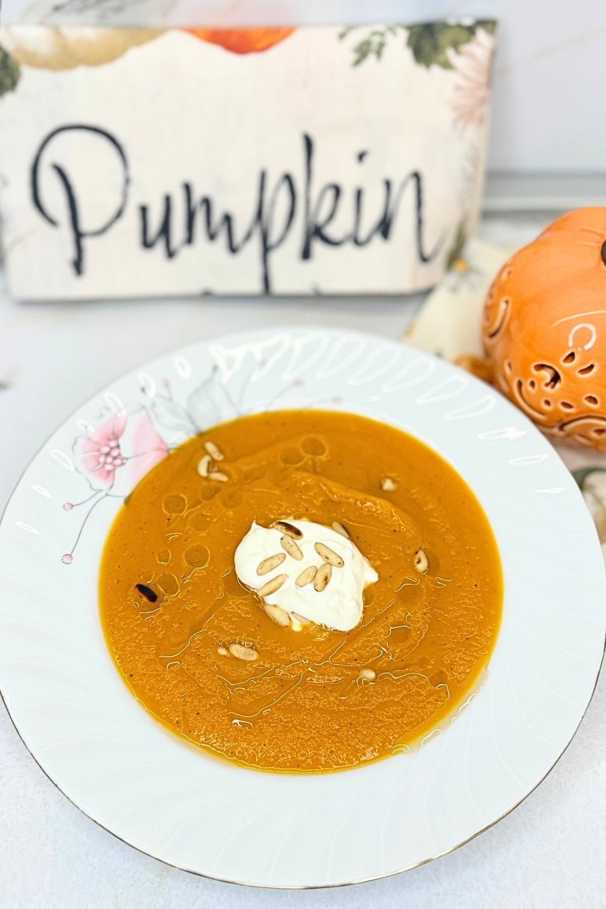 Creamy pumpkin soup topped with sour cream, olive oil, and toasted pine nuts