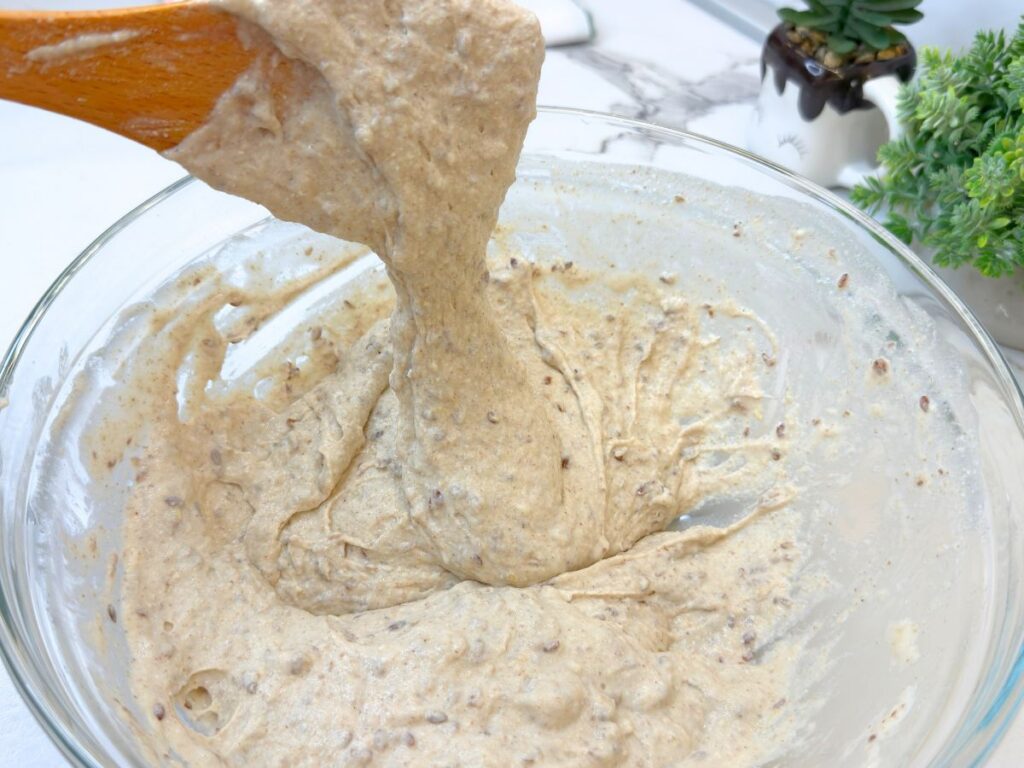 Soft and sticky multigrain roll dough lifted with a wooden spoon to show the correct consistency.