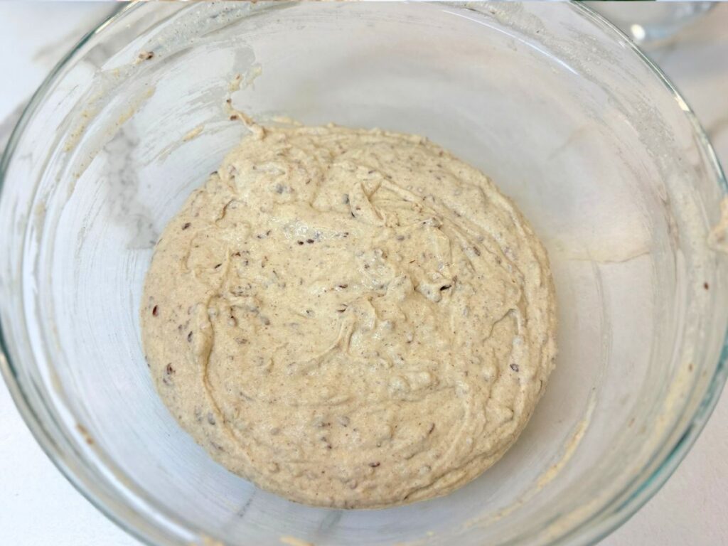 Freshly mixed gluten-free multigrain dough resting in a glass bowl before rising.