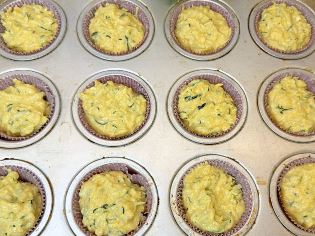 Zucchini muffin batter divided among paper liners in a standard muffin pan.