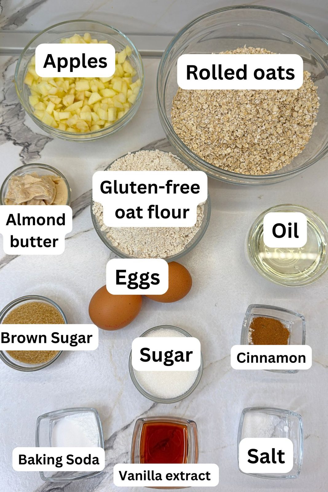 Ingredients for gluten-free apple oatmeal cookies, including apples, oats, oat flour, almond butter, eggs, and cinnamon