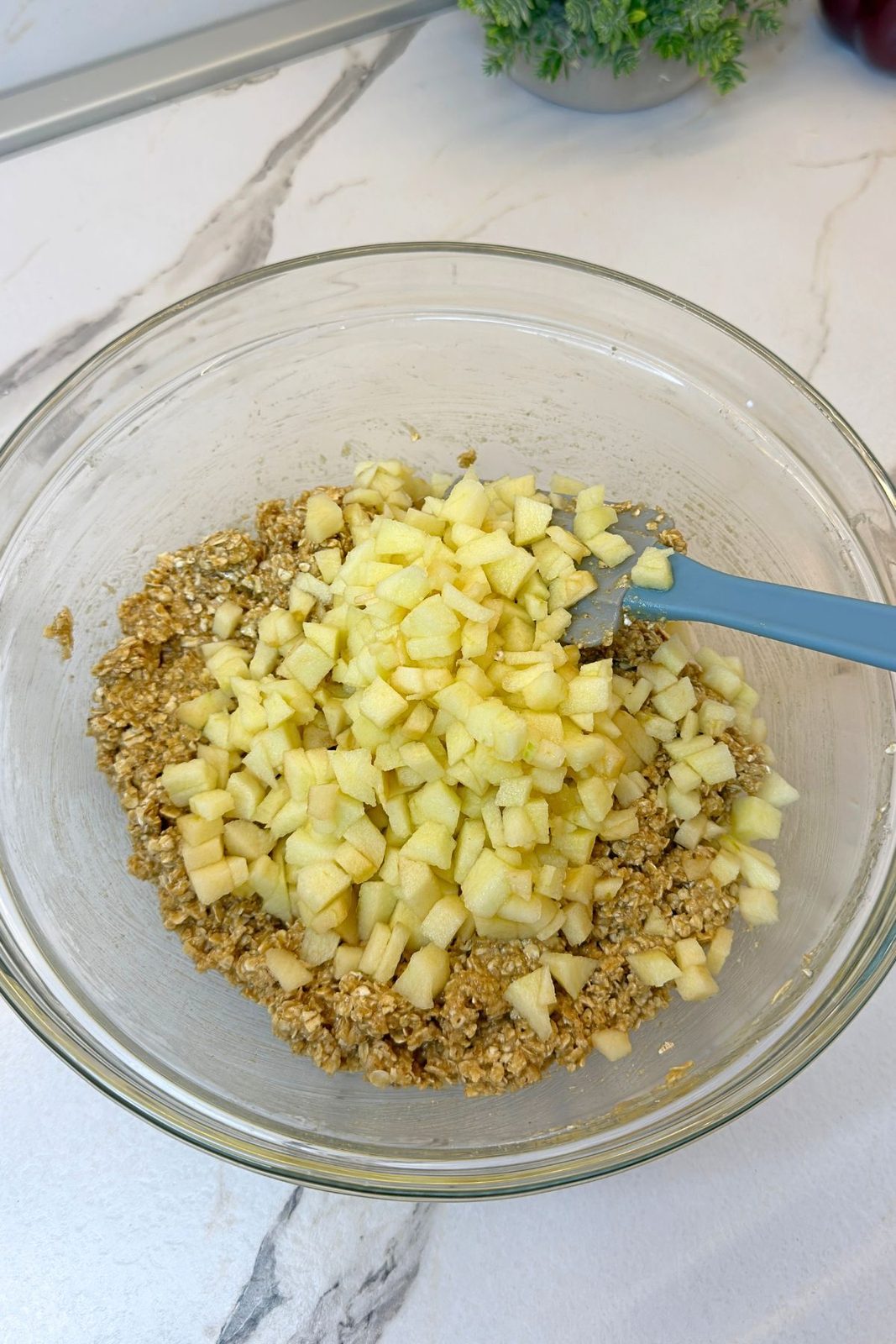Finely diced apples added to oatmeal cookie dough in a glass mixing bowl
