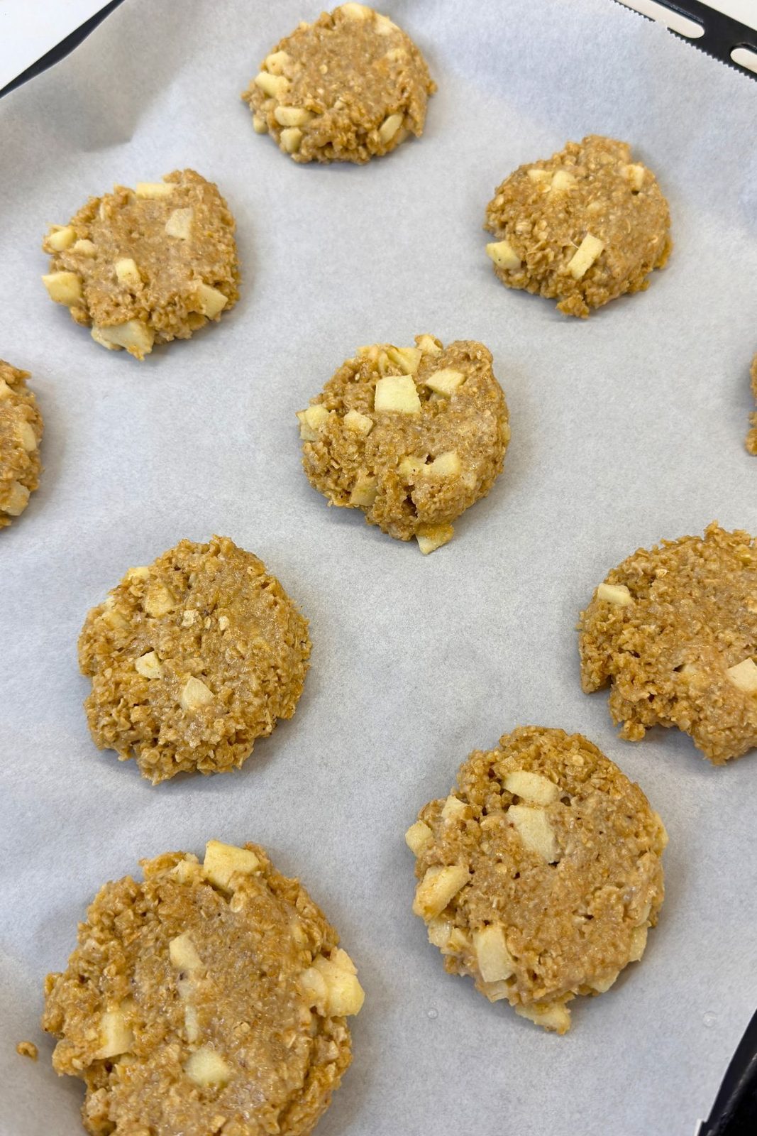 Flattened apple oatmeal cookie dough portions on a parchment-lined baking sheet
