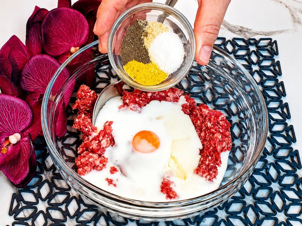 Ground beef combined with egg, yogurt, and seasonings in a glass mixing bowl