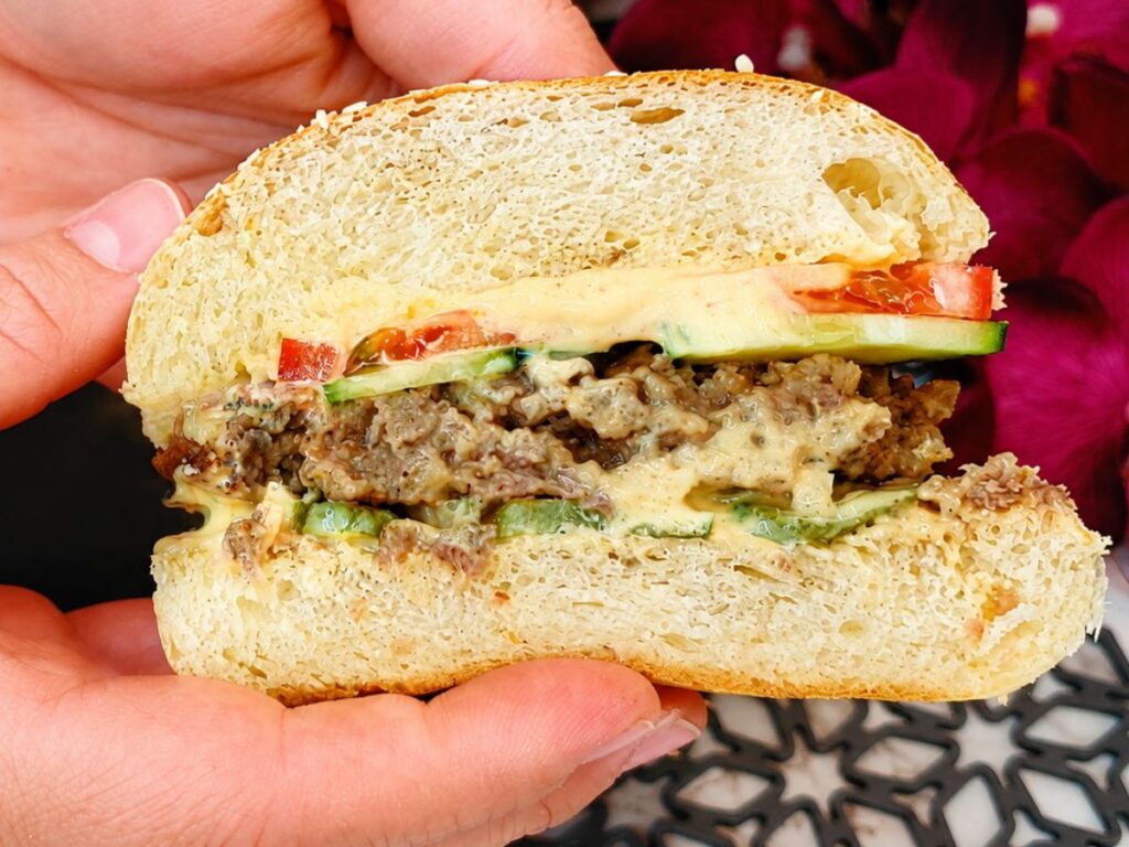 Juicy homemade burger held open to show the beef patty, creamy sauce, and fresh vegetables