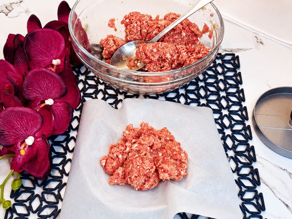 Burger patty mixture portioned onto parchment paper beside a burger press