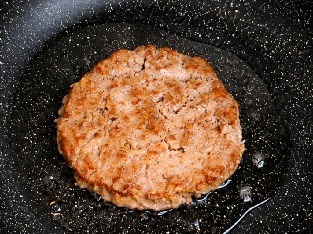 Homemade burger patty cooking until golden brown in a skillet