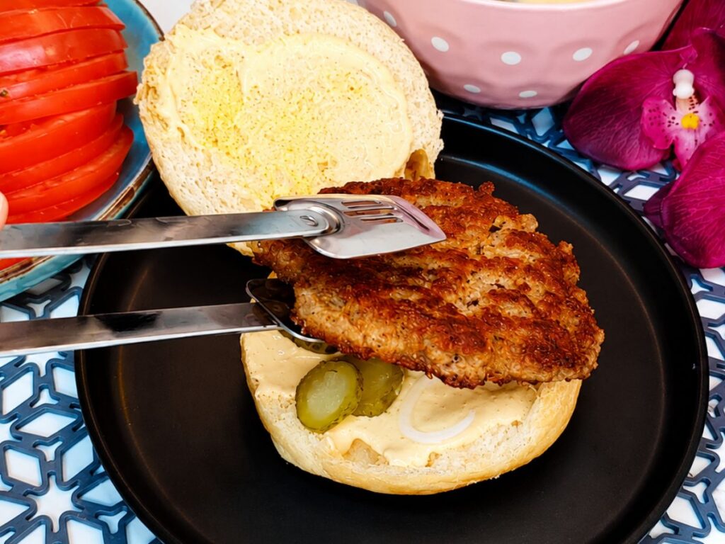 Cooked burger patty placed on a sauced homemade bun with pickle slices