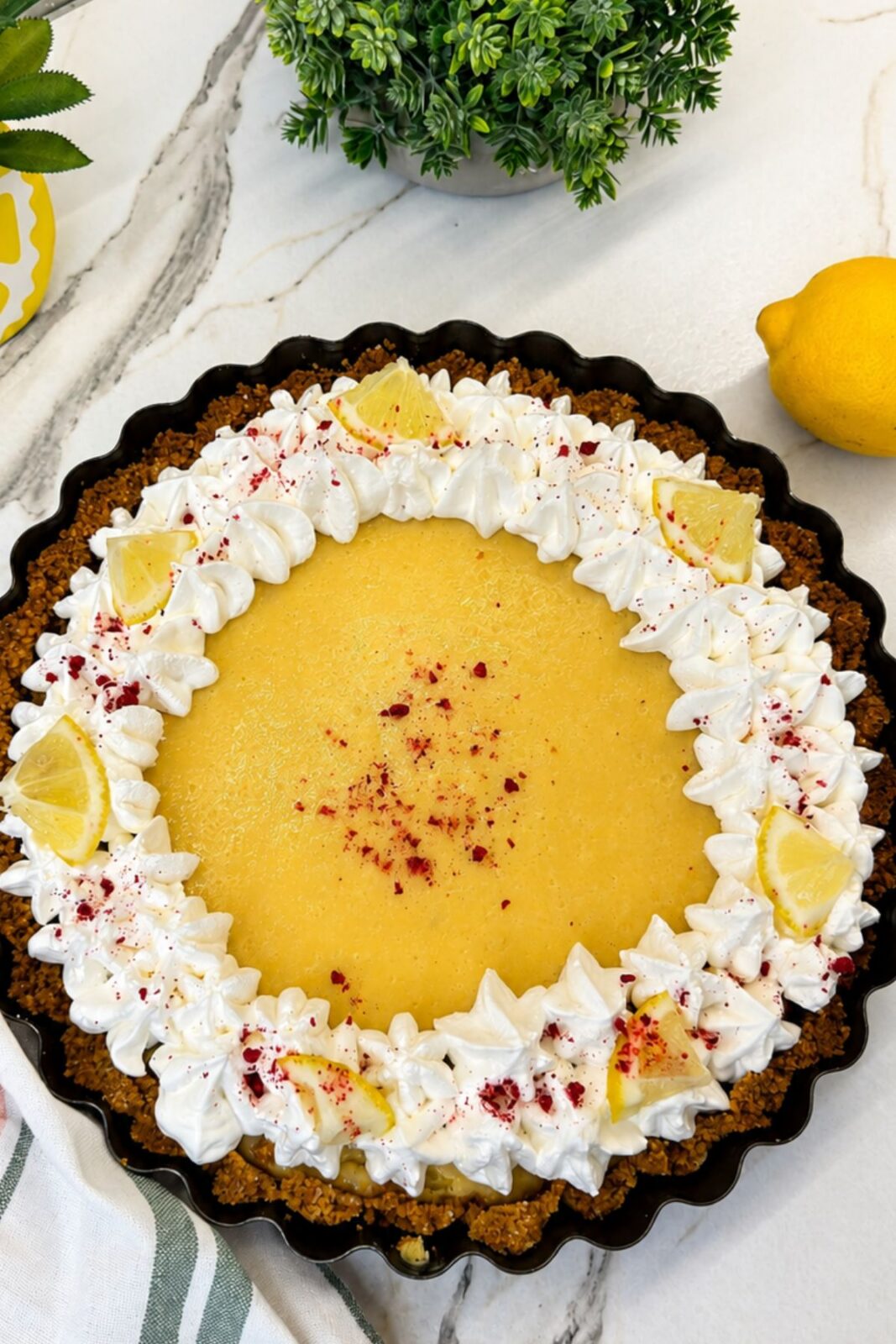 Creamy lemon pie decorated with whipped cream, lemon slices, and dried raspberries