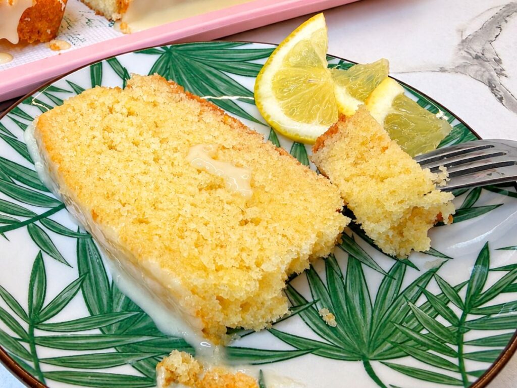 Moist slice of lemon pound cake with lemon glaze and fresh lemon wedges