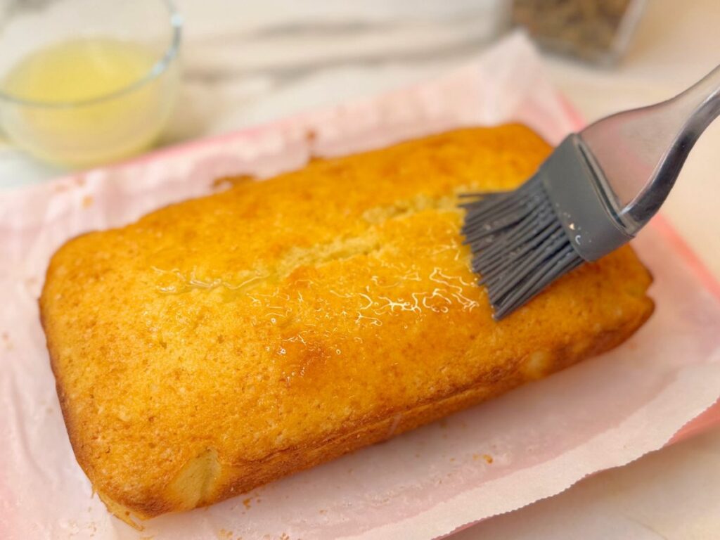 Warm lemon pound cake being brushed with homemade lemon syrup