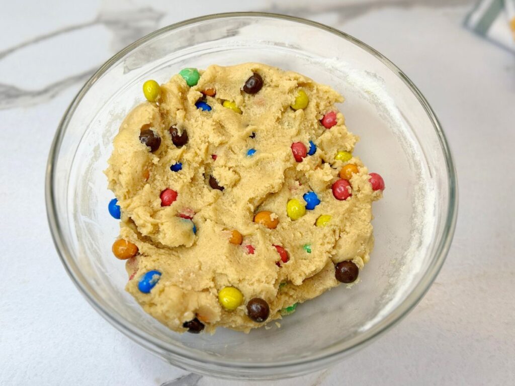 M&M cookie dough mixed with colorful M&M candies in a bowl.