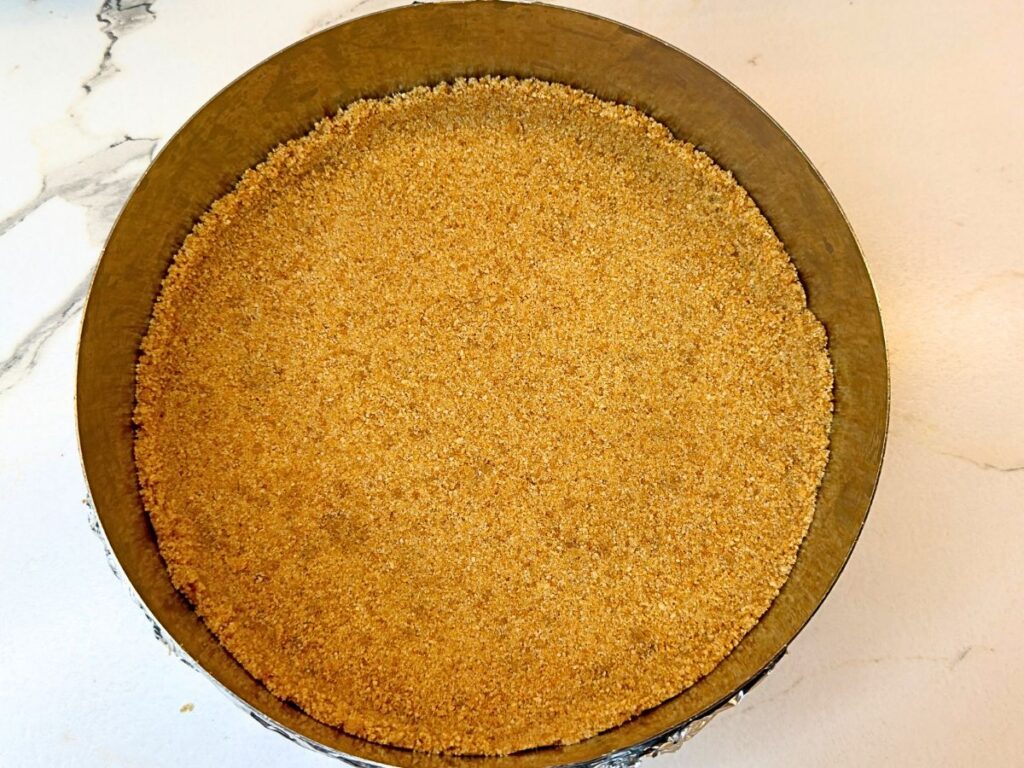 Cookie crumb crust pressed evenly into a springform pan and ready to bake