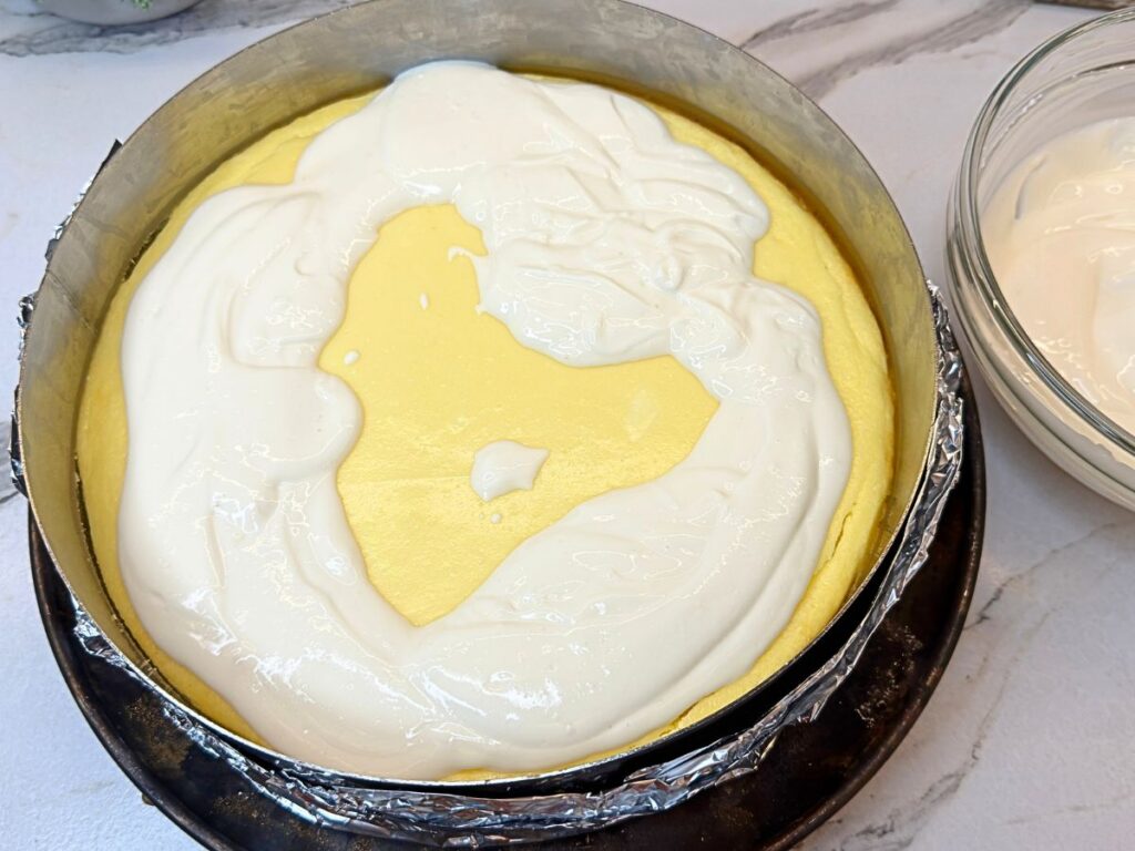 Sour cream topping being spread over the warm baked cheesecake