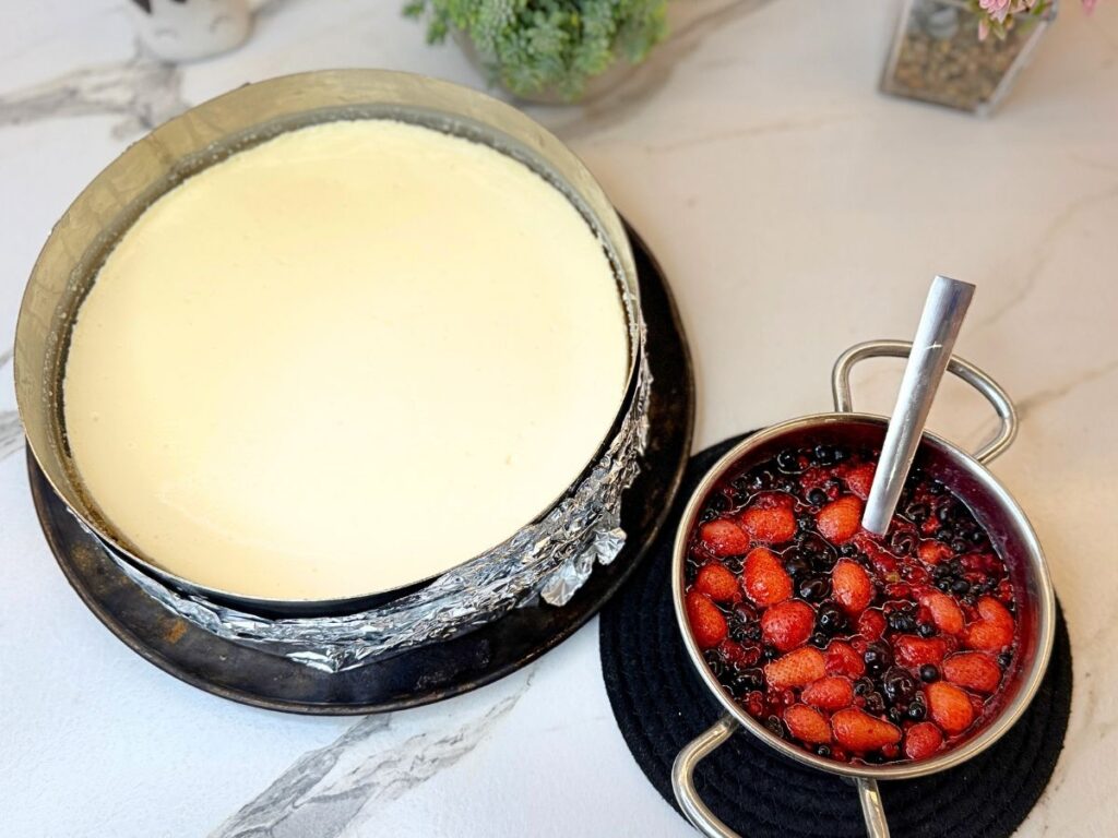 Chilled cheesecake beside a saucepan of homemade mixed berry topping