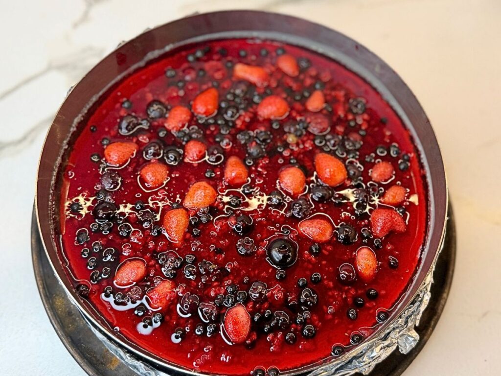 Glossy mixed berry topping spread over the chilled cheesecake